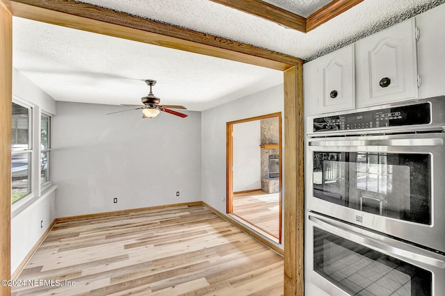 kitchen with light wood finished floors, stainless steel double oven, white cabinets, ceiling fan, and a textured ceiling