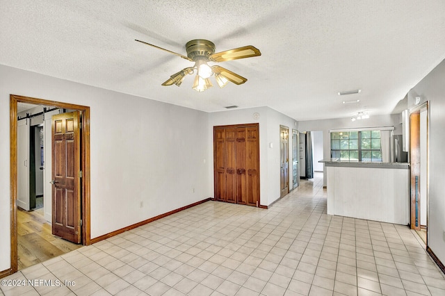 unfurnished room with visible vents, a barn door, a textured ceiling, and a ceiling fan