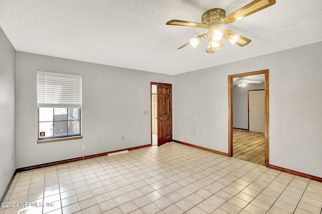 empty room featuring ceiling fan, a textured ceiling, baseboards, and light tile patterned floors