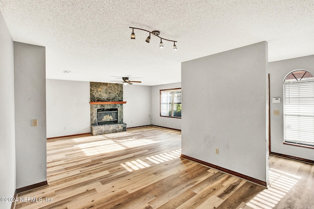 unfurnished living room with a textured ceiling, a fireplace, a ceiling fan, and wood finished floors