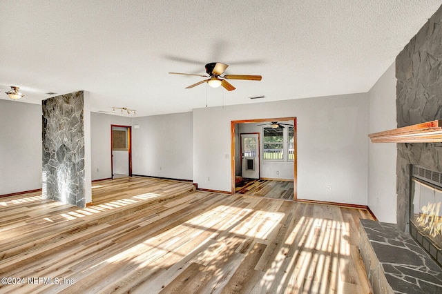 unfurnished living room with a textured ceiling, a fireplace, visible vents, a ceiling fan, and hardwood / wood-style floors