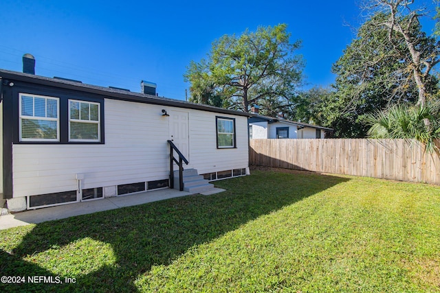 back of property with entry steps, fence, and a yard