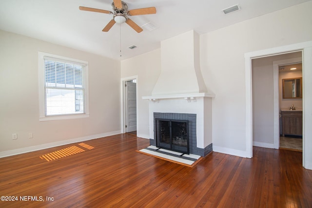 unfurnished living room with a brick fireplace, wood-type flooring, visible vents, and baseboards