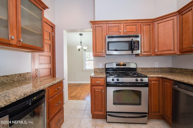 kitchen featuring light tile patterned floors, appliances with stainless steel finishes, glass insert cabinets, and light stone counters