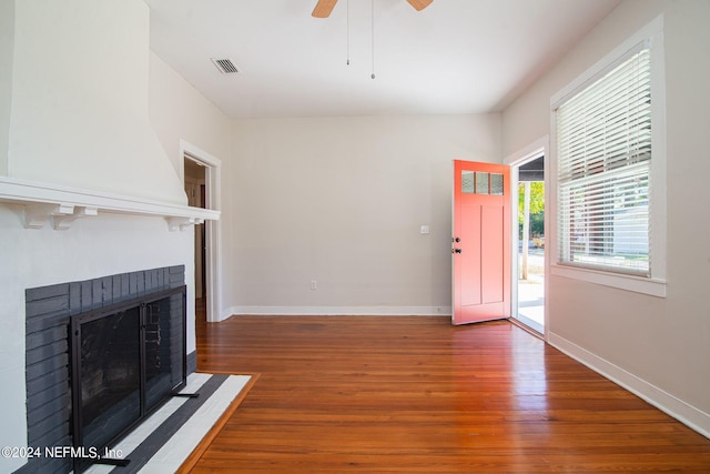 foyer with a brick fireplace, wood finished floors, visible vents, and baseboards