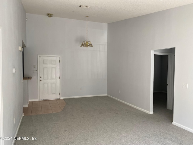 spare room featuring a towering ceiling, carpet floors, a textured ceiling, and an inviting chandelier