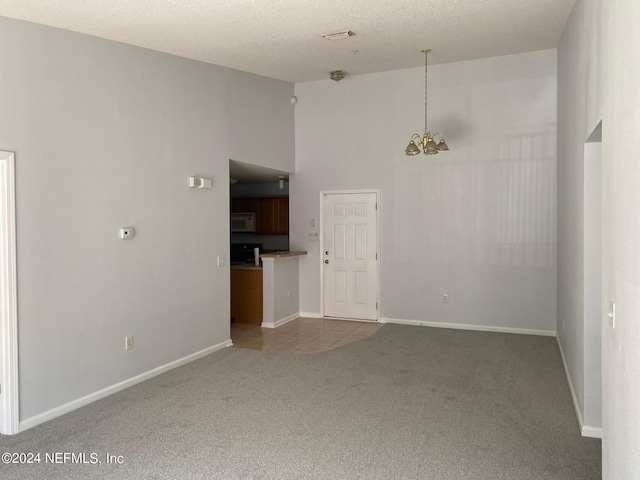 unfurnished room featuring a textured ceiling, a towering ceiling, light colored carpet, and a notable chandelier