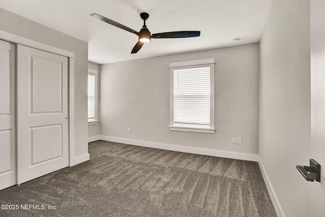 unfurnished bedroom with ceiling fan, a textured ceiling, a closet, and dark colored carpet