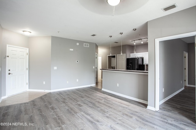 kitchen featuring light wood-type flooring, rail lighting, black fridge, white cabinets, and hanging light fixtures