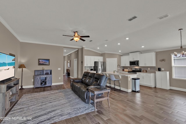 living room featuring ceiling fan with notable chandelier, sink, crown molding, and vaulted ceiling