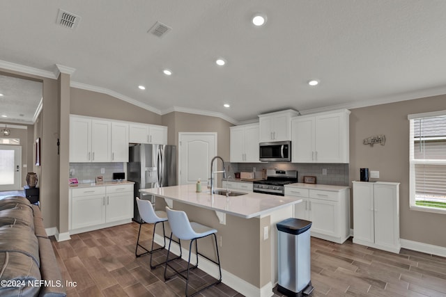 kitchen with a kitchen island with sink, sink, vaulted ceiling, white cabinetry, and stainless steel appliances