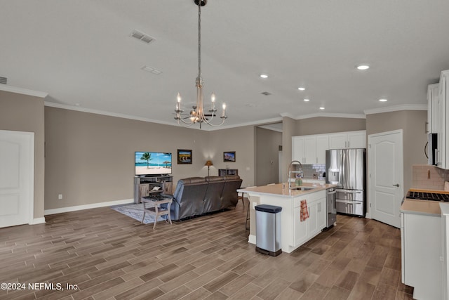 kitchen with decorative backsplash, stainless steel fridge, a kitchen island with sink, sink, and decorative light fixtures