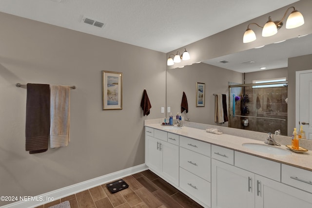 bathroom with vanity, a shower with shower door, and a textured ceiling