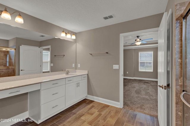 bathroom with a textured ceiling, vanity, walk in shower, and ceiling fan