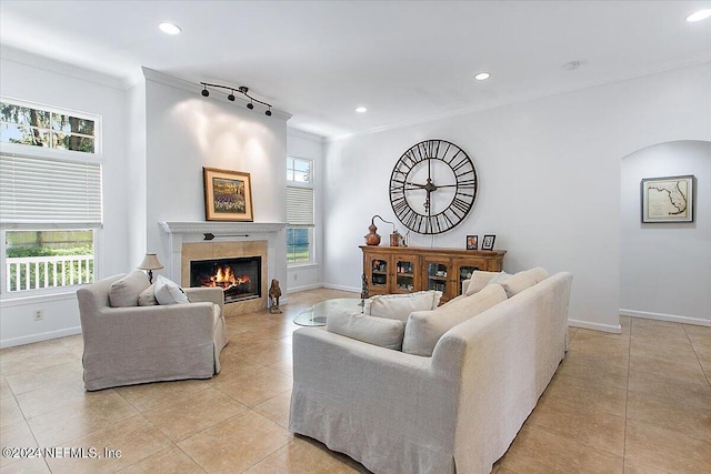 living room featuring a tile fireplace, light tile patterned floors, rail lighting, and ornamental molding