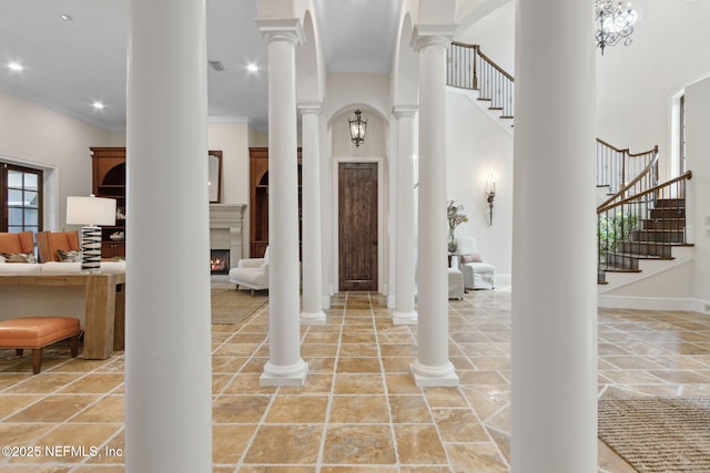 foyer featuring a lit fireplace, ornamental molding, stairway, and ornate columns