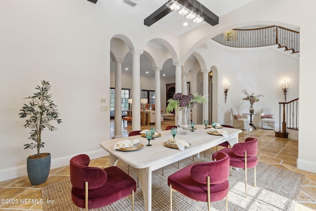 dining room featuring arched walkways, baseboards, ceiling fan, a high ceiling, and ornate columns