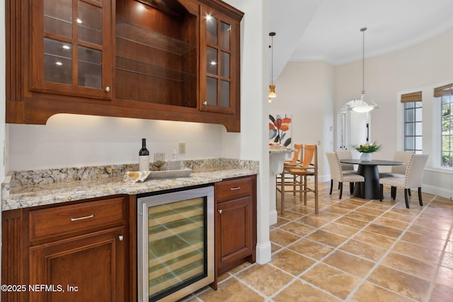 bar featuring wine cooler, decorative light fixtures, ornamental molding, a bar, and baseboards