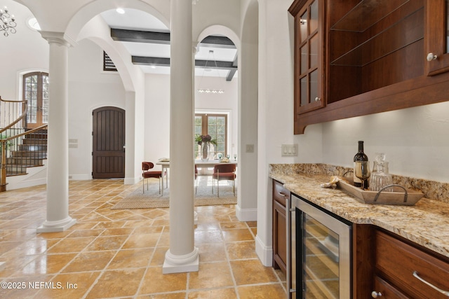 bar with arched walkways, beverage cooler, baseboards, a dry bar, and decorative columns