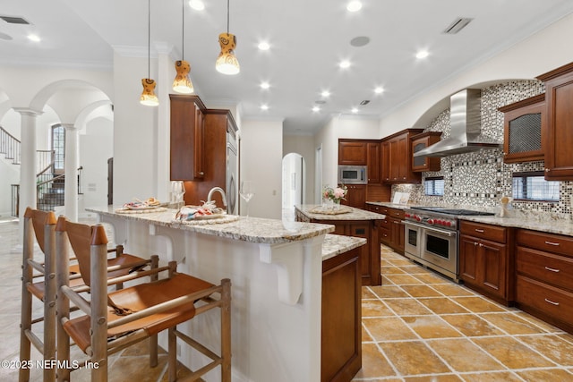 kitchen with arched walkways, decorative light fixtures, a breakfast bar area, stainless steel appliances, and wall chimney range hood