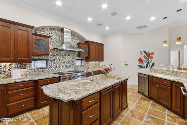 kitchen with wall chimney exhaust hood, an island with sink, a sink, and decorative light fixtures