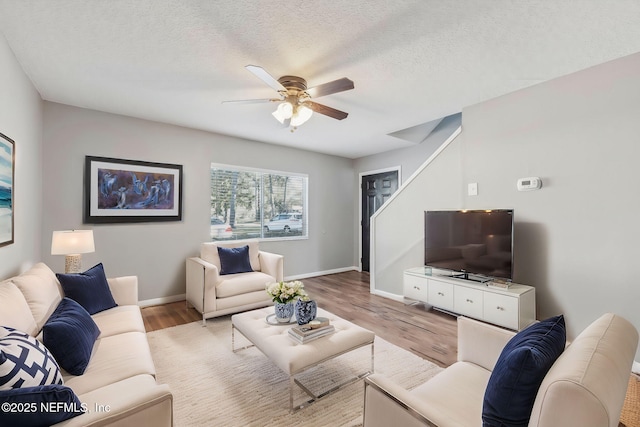 living area with baseboards, light wood-style floors, ceiling fan, and a textured ceiling
