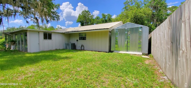 rear view of house featuring a lawn, central AC unit, and an outbuilding