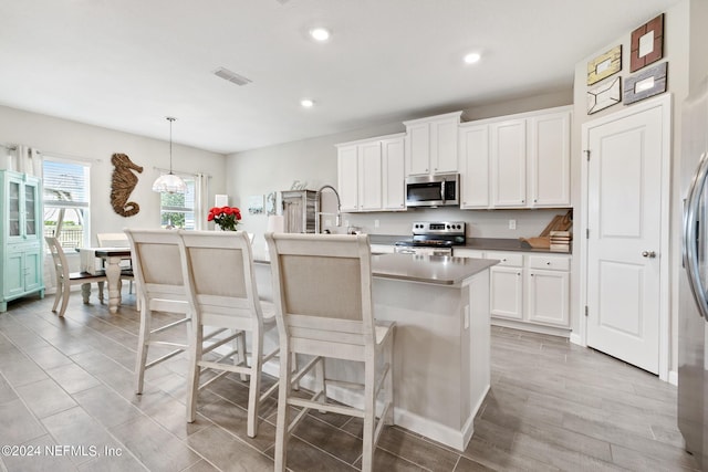 kitchen with white cabinets, appliances with stainless steel finishes, hanging light fixtures, and an island with sink