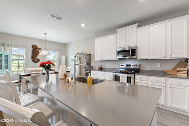 kitchen with sink, decorative light fixtures, a kitchen bar, a kitchen island with sink, and appliances with stainless steel finishes