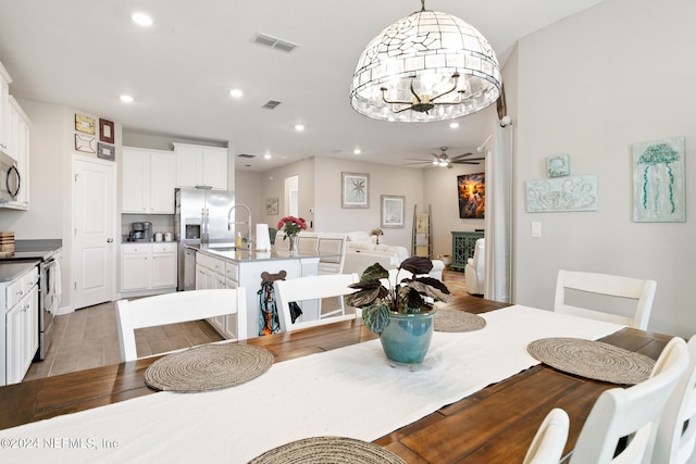 dining room featuring ceiling fan with notable chandelier, a fireplace, sink, and light hardwood / wood-style flooring