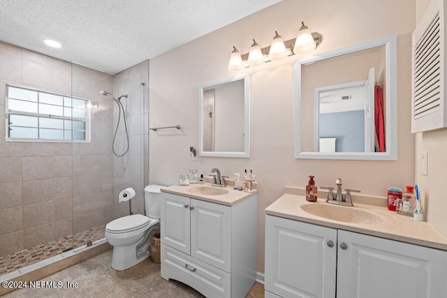 bathroom featuring vanity, a tile shower, toilet, and a textured ceiling