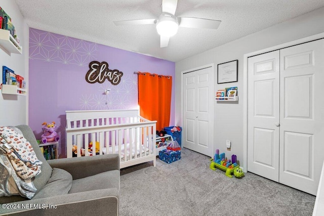 carpeted bedroom featuring a textured ceiling, ceiling fan, and a crib