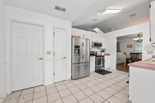 kitchen featuring hanging light fixtures, white cabinets, lofted ceiling, light tile patterned floors, and appliances with stainless steel finishes