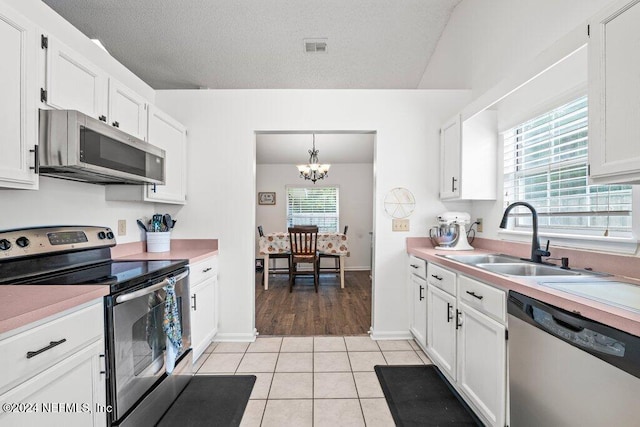 kitchen with a wealth of natural light, sink, stainless steel appliances, decorative light fixtures, and white cabinets