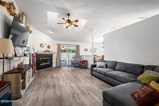 living room featuring a fireplace, hardwood / wood-style floors, lofted ceiling with skylight, a textured ceiling, and ceiling fan