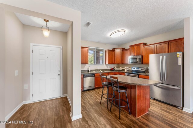 kitchen featuring dark hardwood / wood-style flooring, a kitchen island, sink, a kitchen bar, and appliances with stainless steel finishes