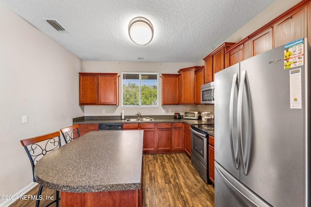 kitchen with a textured ceiling, a kitchen island, appliances with stainless steel finishes, dark hardwood / wood-style floors, and sink