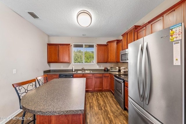 kitchen featuring visible vents, dark countertops, appliances with stainless steel finishes, dark wood-type flooring, and a sink