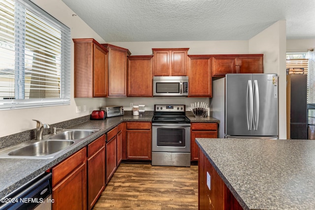 kitchen with dark countertops, appliances with stainless steel finishes, dark wood-type flooring, a textured ceiling, and a sink