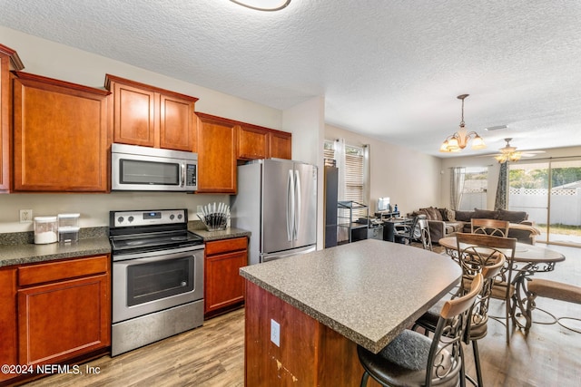 kitchen with stainless steel appliances, light hardwood / wood-style flooring, a textured ceiling, and ceiling fan with notable chandelier