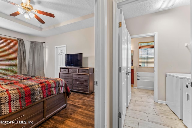 bedroom with ceiling fan, wood finished floors, independent washer and dryer, a tray ceiling, and a textured ceiling