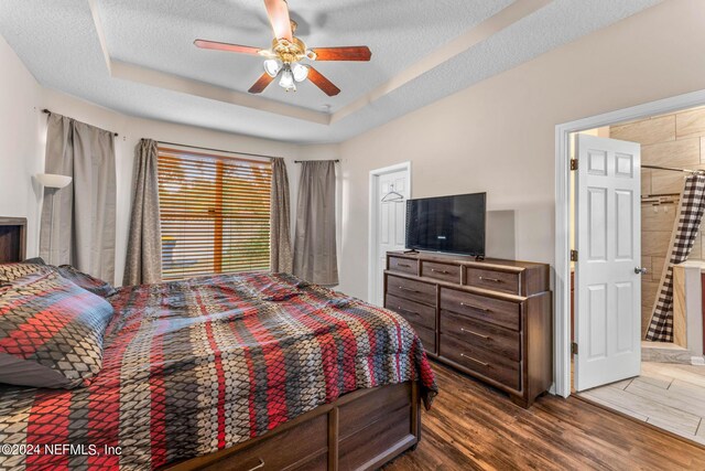 bedroom featuring a tray ceiling, a textured ceiling, dark tile flooring, and ceiling fan