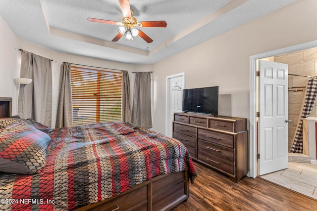 bedroom featuring a ceiling fan, a textured ceiling, a tray ceiling, and dark wood-type flooring