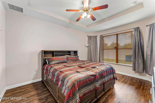 bedroom with a textured ceiling, dark hardwood / wood-style floors, ceiling fan, and a raised ceiling