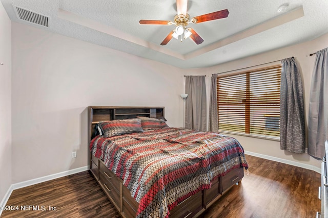 bedroom with a textured ceiling, visible vents, baseboards, dark wood-style floors, and a raised ceiling