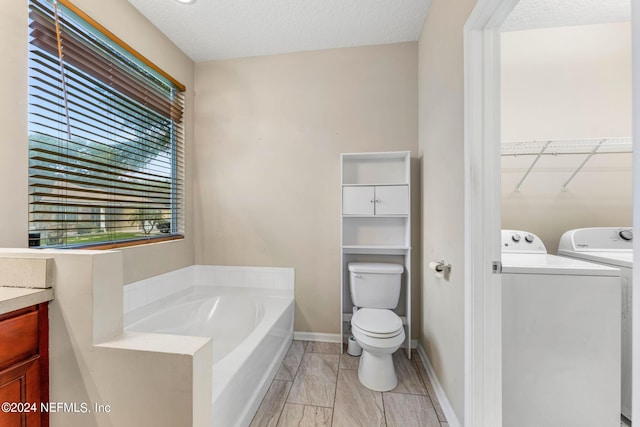 bathroom featuring tile flooring, a tub, washer and dryer, toilet, and vanity