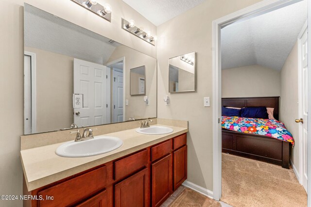 bathroom featuring a textured ceiling, double sink, vaulted ceiling, and vanity with extensive cabinet space