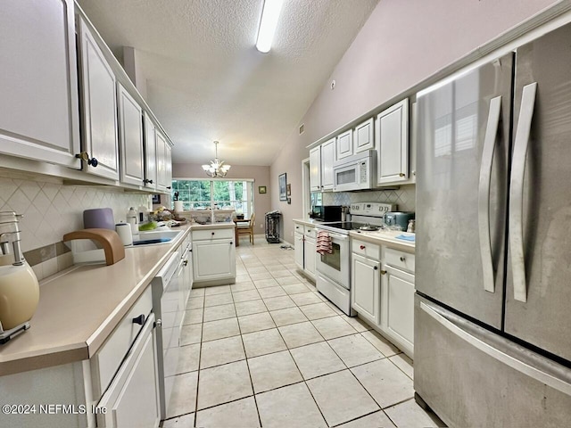 kitchen with lofted ceiling, white appliances, hanging light fixtures, white cabinetry, and a chandelier