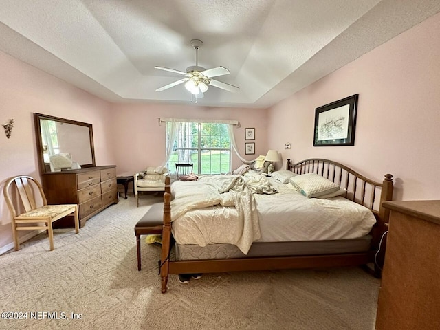 bedroom with light carpet, a textured ceiling, a tray ceiling, and ceiling fan