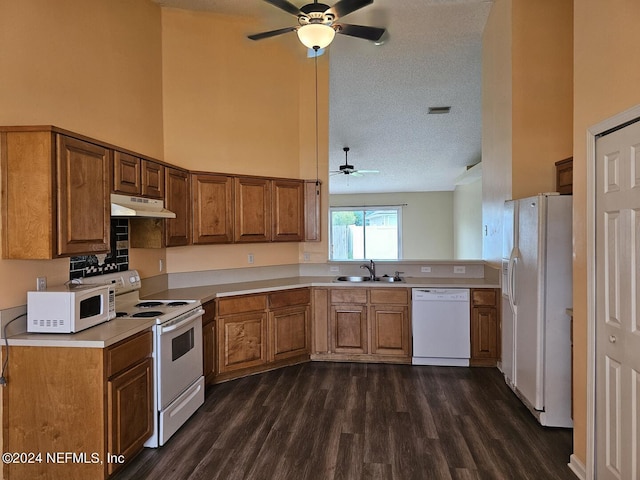 kitchen featuring white appliances, brown cabinets, light countertops, under cabinet range hood, and a sink